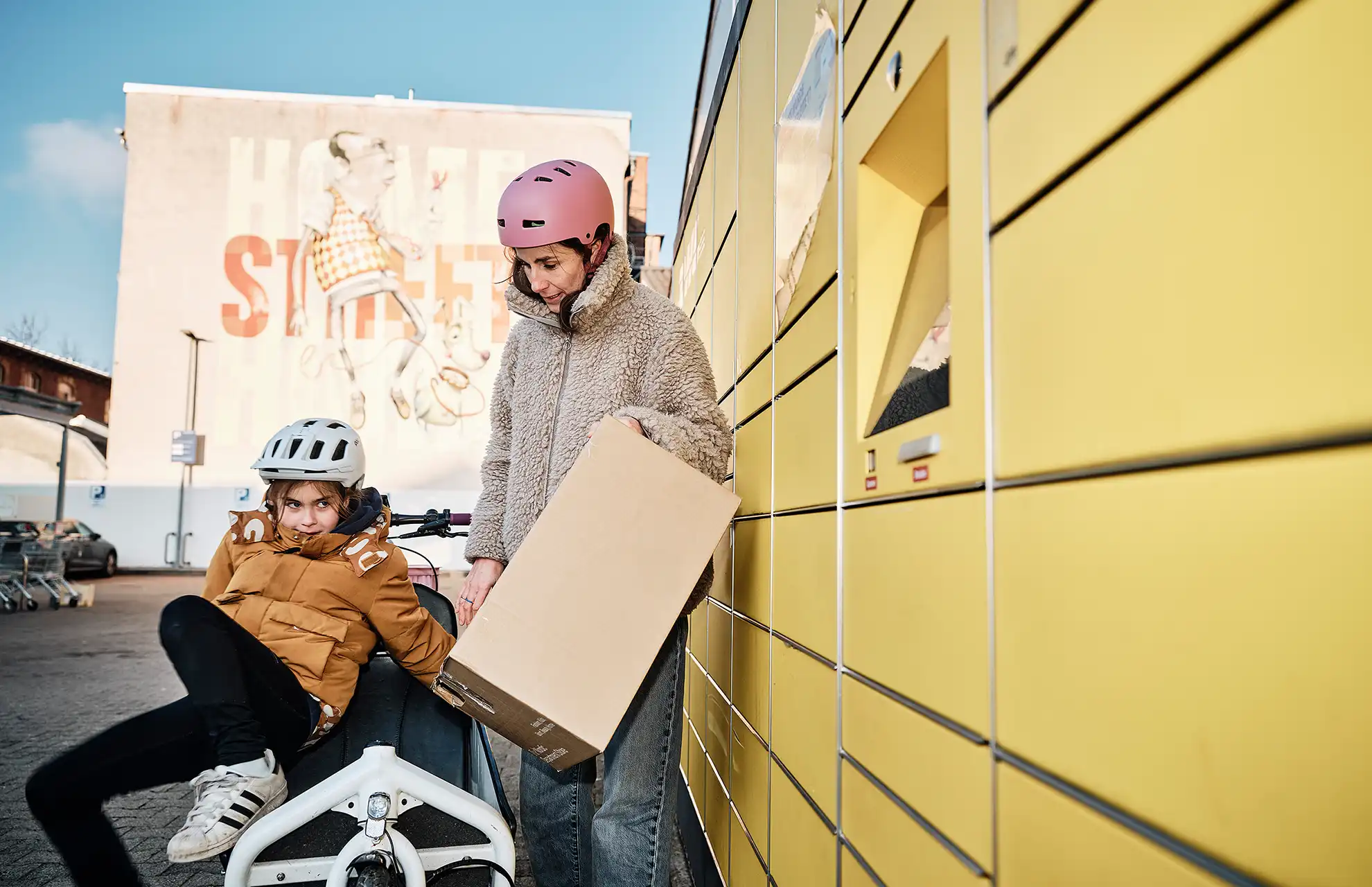 Frau mit Kind und Lastenrad holt Paket an Packstation ab